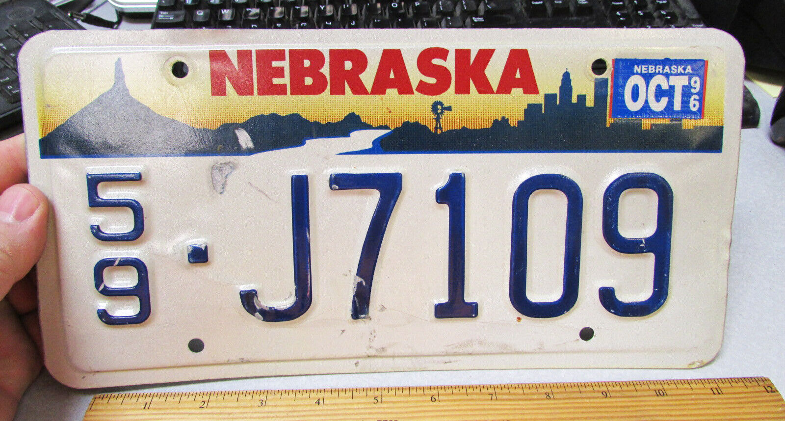 Nebraska Metal License Plate, 1996 exp J7109, chimney rock, city skyline style