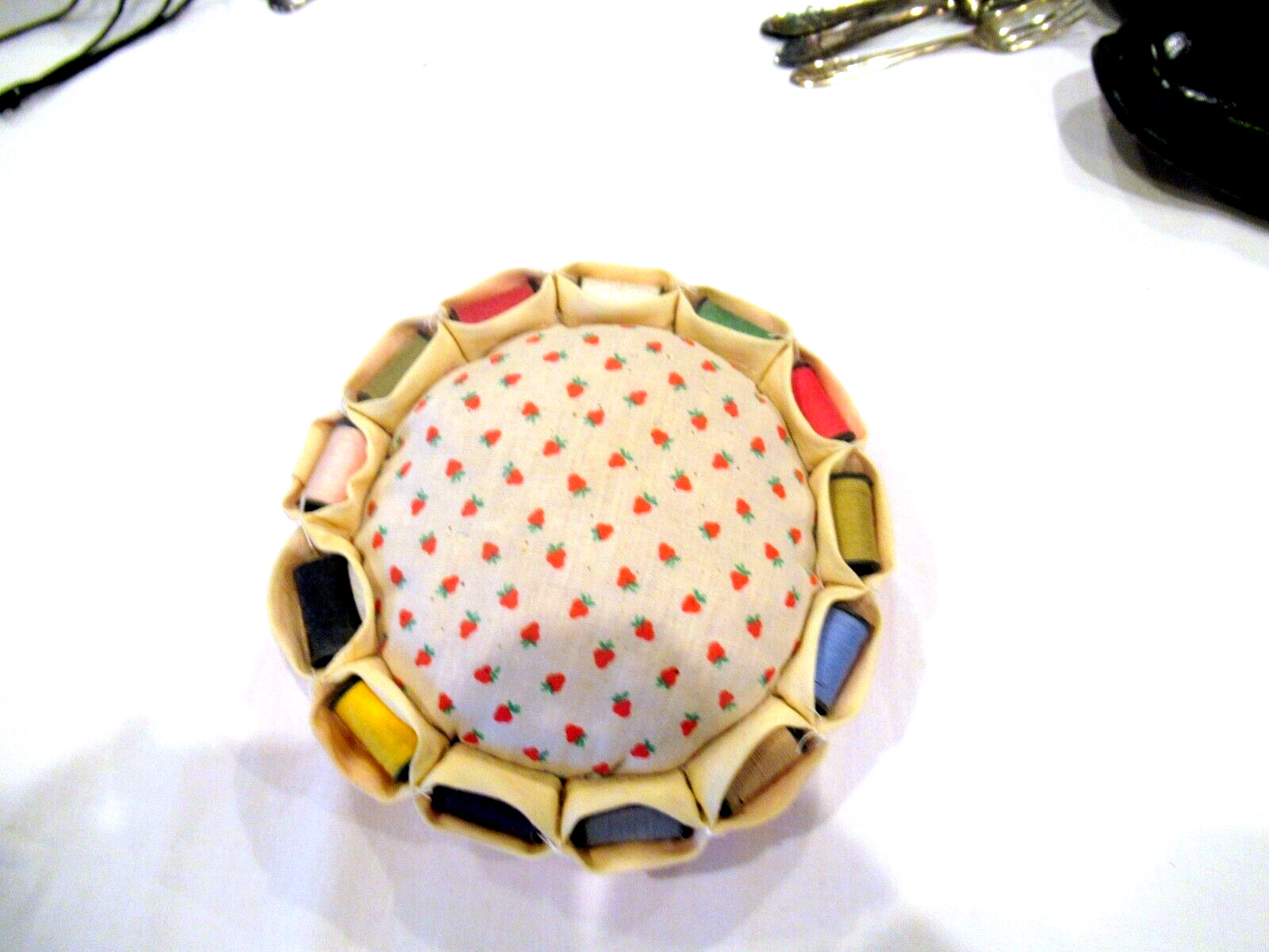 Strawberry pincushion surrounded by 13 spools of thread, c. 1960s