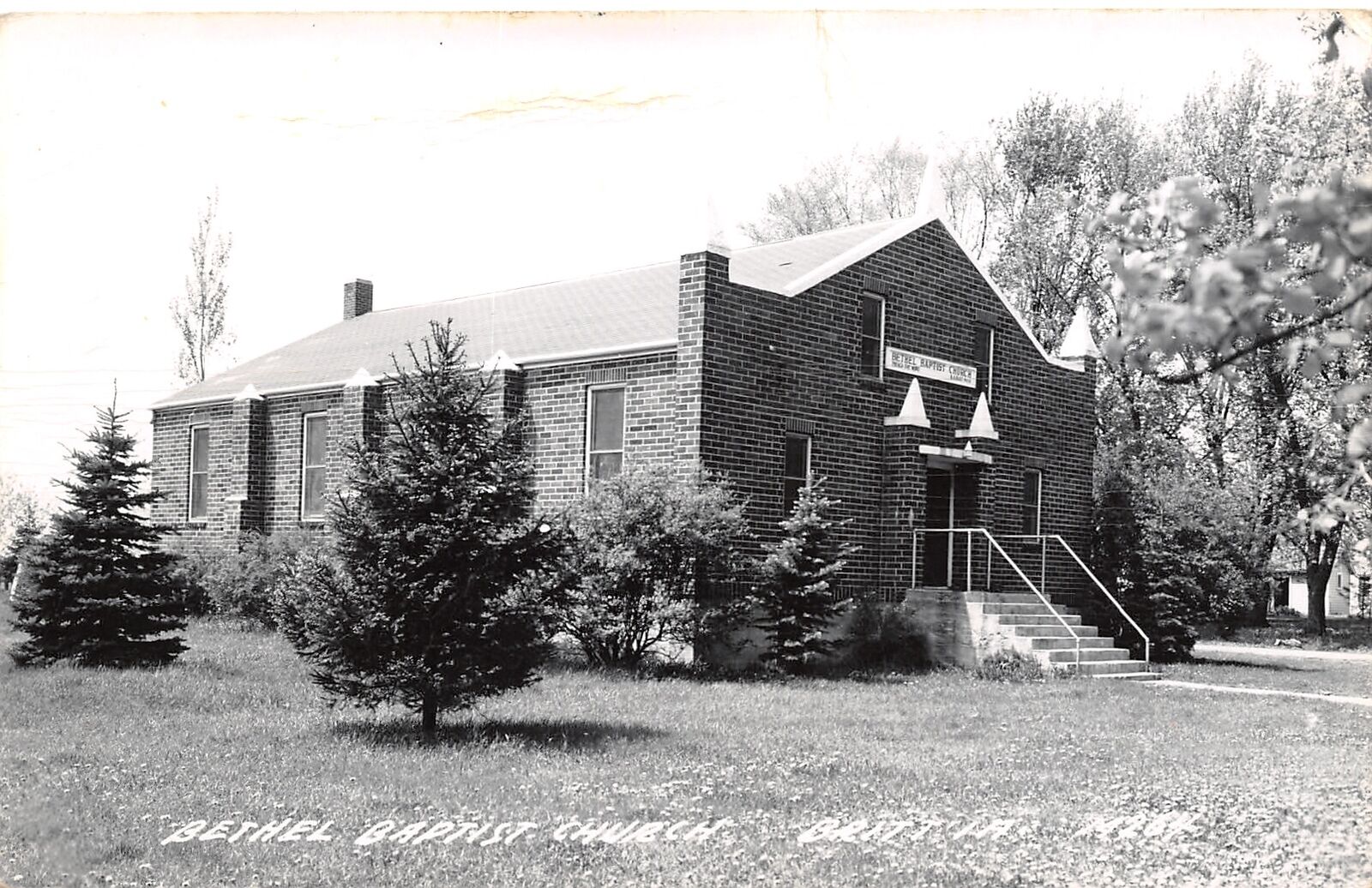 Britt IA Bethel Baptist Church~Brick Facade~Evergreen Trees~Shrubs RPPC c1950