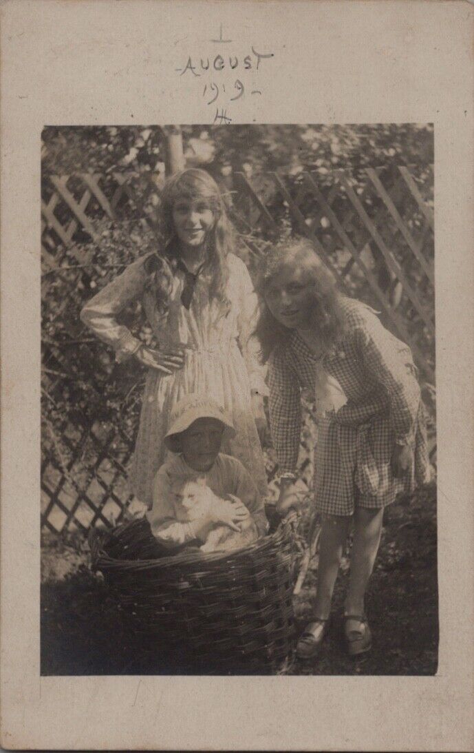 REAL PHOTO POSTCARD RPPC-TWO BLOND SISTERS & BOY IN BASKET HOLDING WHITE CAT