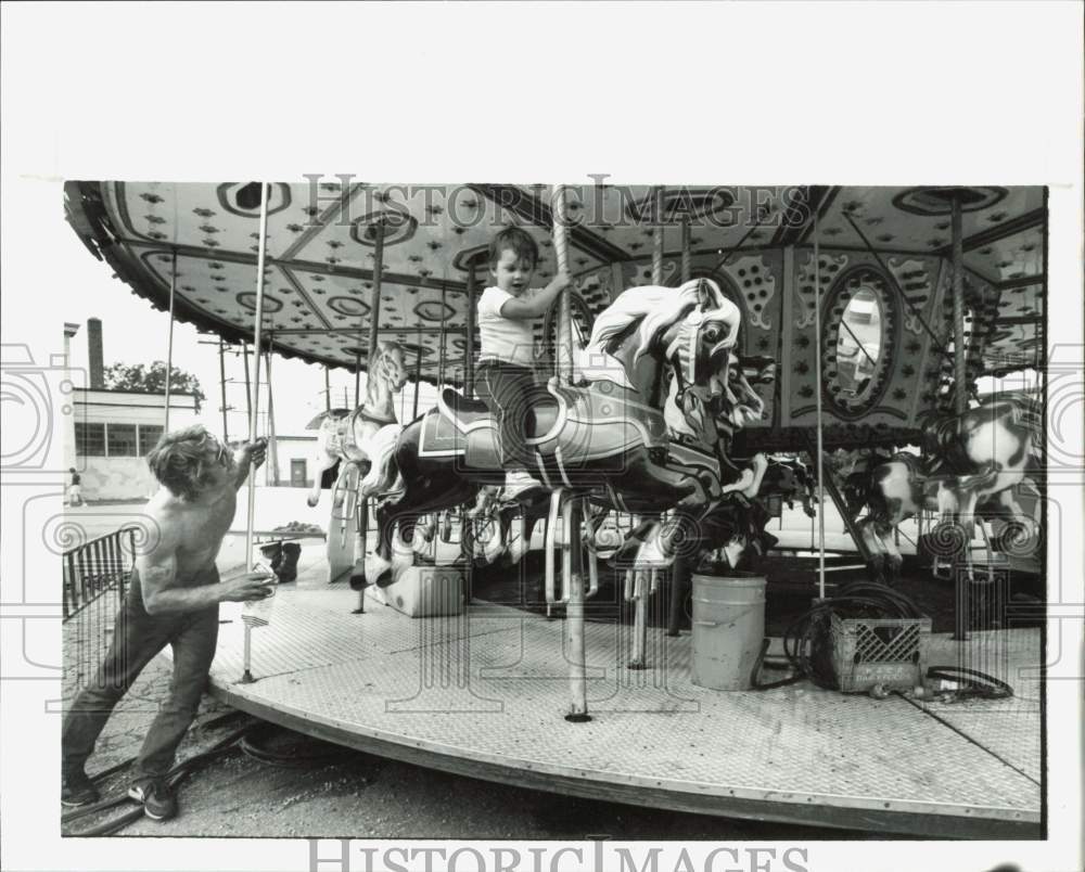1989 Press Photo Boy Rides Merry Go Round While Workers Build It, Michigan