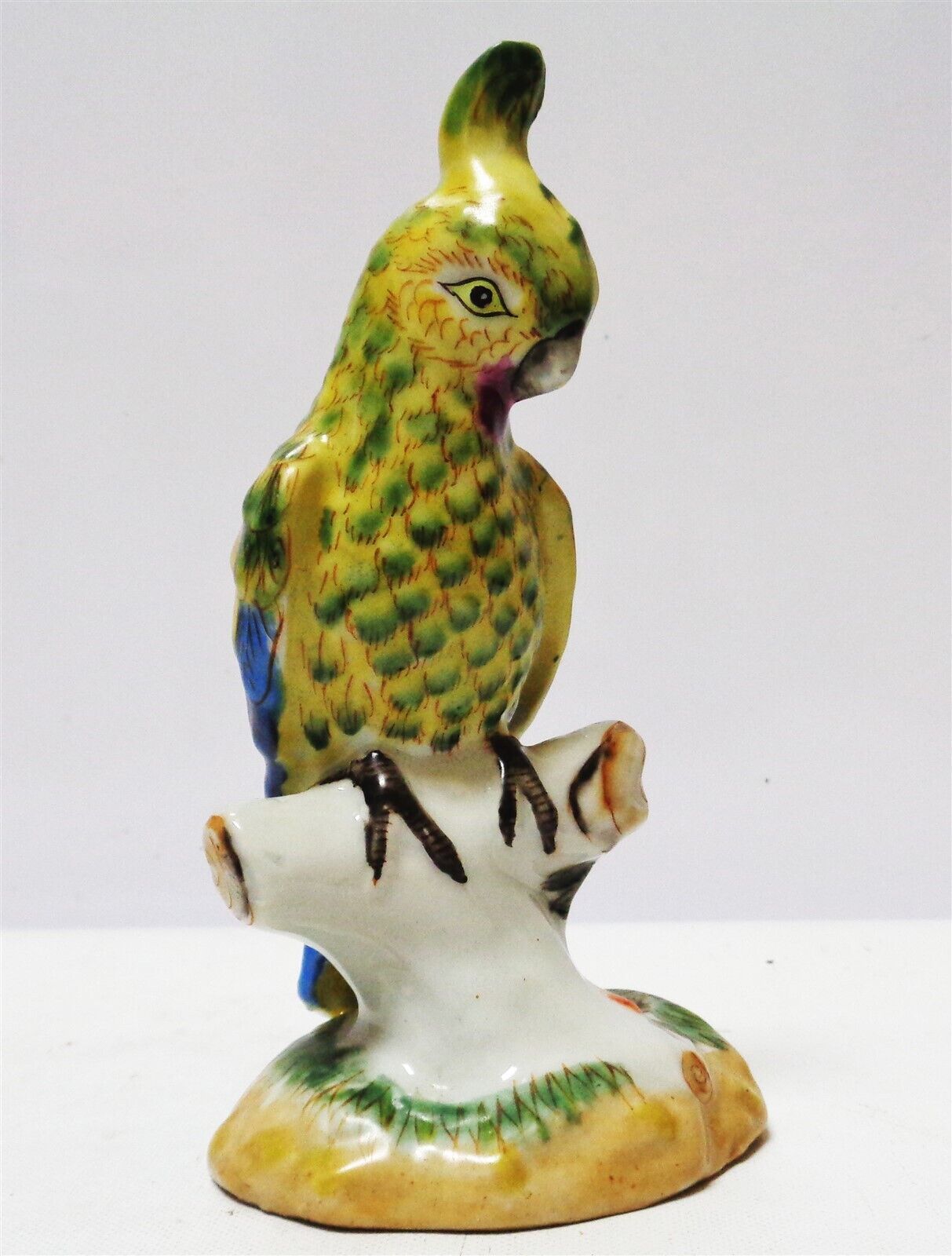 Tozai Home Porcelain Parrot (Green, Tan, & Blue) resting on a branch