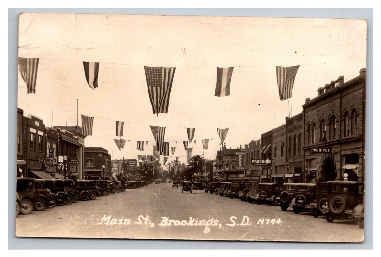 Postcard RPPC Brookings South Dakota Main Street Scene Old Cars Patriotic
