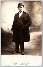 RPPC EARLY 1900S MAN WITH BOWL HAT AND COAT WITH FENCE ON ROAD KRUXO POSTCARD picture