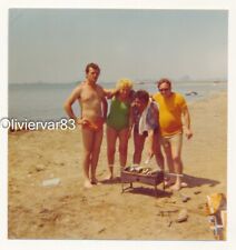 Vintage photo 1975 - man in speedo swimsuit and others do fish barbecue on beach picture