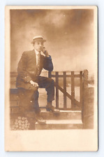 RPPC Photo Postcard Young Man Posing Sitting on Fence Hat Suit Tie c1910-1920 picture