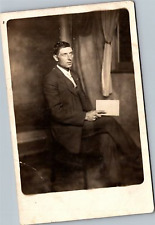 RPPC Man holding book seated in chair by window picture