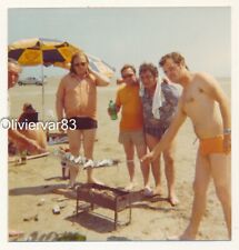 Vintage photo 1975 - man in speedo swimsuit and others do fish barbecue on beach picture